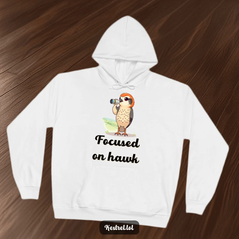 Funny kestrel hoodie with a curious bird using tiny binoculars to scan a landscape. Cozy and humorous apparel.